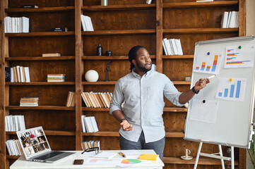 Wall Mural - African businessman talking to colleague team in video call conference in the cabinet at home office, explains his idea by showing the graphs on the white board, using laptop for online meeting