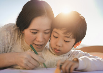 asian mother doing drawing activities with little son outdoor on patio - parent and child having fun