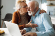 © Goran - Mature woman kissing her mature husband while he uses a computer at home
