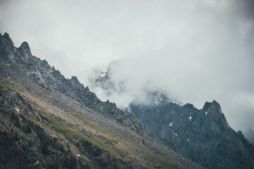 dark atmospheric surreal landscape with dark rocky mountain top in low clouds in gray cloudy sky. gr