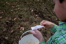 Outdoor Lifestyle Portrait Of The Side Of A Young Boys Face Who Is Wearing A Green Plaid Shirt Holding An Easter Bucket And Reading A Clue During An Easter Scavenger Hunt