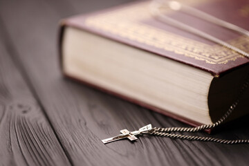 Silver necklace with crucifix cross on christian holy bible book on black wooden table. Asking blessings from God with the power of holiness, which brings luck