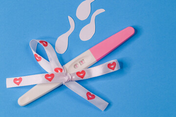 Pregnancy test with tape.
Pregnancy test with ribbon with hearts and cut out paper sperm on a blue background, top view close-up.