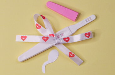 
Pregnancy test with tape.
Pregnancy test with ribbon with hearts and cut out paper sperm on a yellow pastel background, top view close-up.