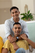 © wavebreak3 - Portrait of diverse gay male couple sitting on sofa looking at camera and smiling