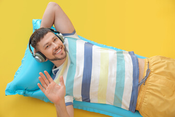 Wall Mural - Handsome man listening to music while lying on inflatable mattress against color background