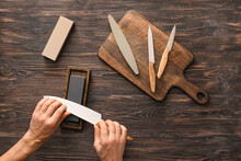 Man Sharpening Knife On Wooden Background
