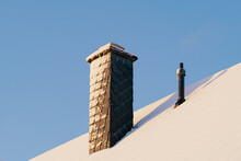 Snow Covered Roof And Chimney Against Sky