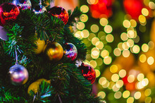 Selective Focus Of Baubles Hanging On Christmas Tree With Colorful Bokeh Background.