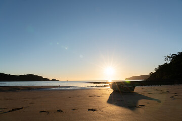 Sticker - Dinghy sitting on sand at low tide in silhouette backlit by setting sun.