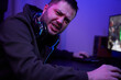 © snedorez - Gamer or streamer in headphones with microphone sits at home in neon light and plays at pc