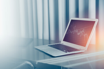 laptop computer on office desk with stock chart blue color tone for money business background.