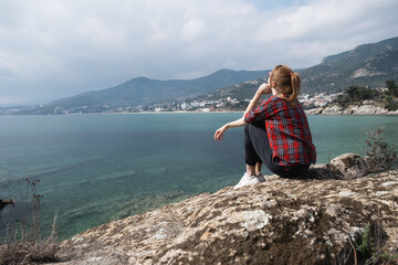 Young woman sitting on the edge and observing beautiful nature landscape with calm sea and island at background