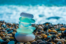 Sea Glass Stones Arranged In A Balance Pyramid On The Beach. Beautiful Azure Color Sea With Blurred Seascape Background. Meditation And Harmony Concept.