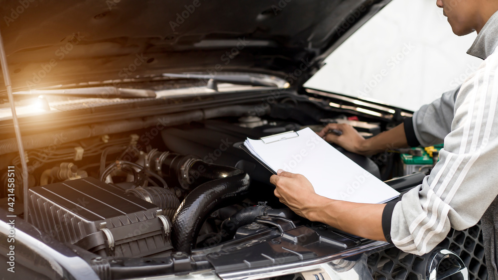 Automobile mechanic repairman checking a car engine with inspecting writing to the clipboard the checklist for repair machine, car service and maintenance.