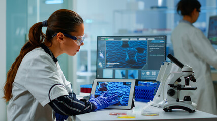 Wall Mural - Scientist using digital tablet analysing virus evolution, treatment development in medical research laboratory. Medicine, biotechnology research in advanced pharma lab, examining vaccine evolution