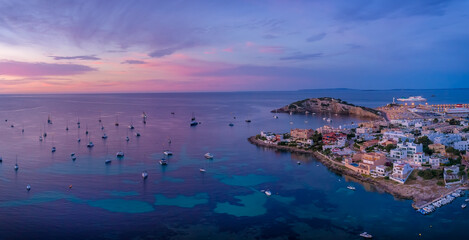 Amazing sunset in Ibiza Spain with orange and violet sky and boats floating on the sea and coast view of the town