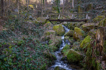 Sticker - Old wooden bridge with water cascade flowing through big rocks in the forest