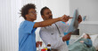 © TommyStockProject - Indian doctor and african intern studying x-ray of patient in hospital ward