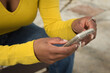 © Manuel - Detail of hands of african american woman in yellow t-shirt consulting her cell phone.