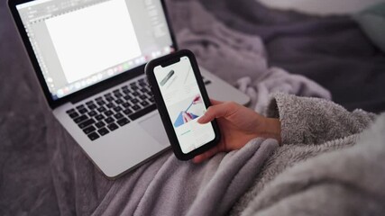 Wall Mural - Young woman does online shopping with smartphone in bed and laptop on her lap.