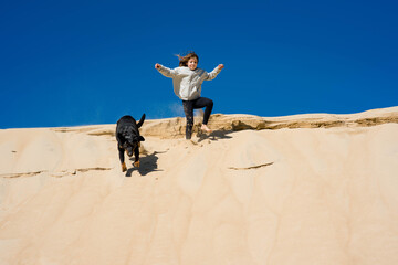 Wall Mural - cute little girl running with her dog in the sand dunes