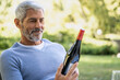 © PhotoAlto - Smiling mature man looking at wine bottle while sitting on chair