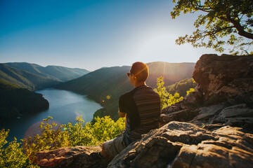 Traveler enjoying sunset on a cliff with a beautiful view of a lake. 