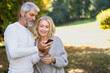 © PhotoAlto - Smiling mature couple using smartphone in backyard