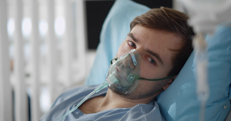 young attractive man with oxygen mask looking sad and worried lying at hospital bed