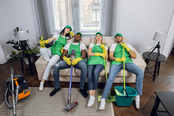 Wall Mural - Tired multiracial cleaners relaxing together on couch