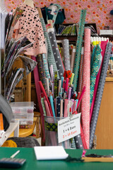 In a fabric shop, colorful fabrics are rolled up in rolls. Buttons in the containers, on the table: pens, calculators, notepads, magazines in the compartments.