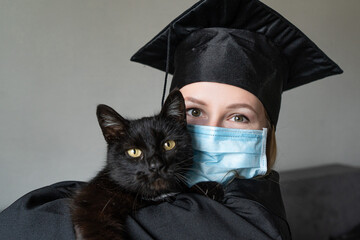 Graduation of a woman with face mask dressed in a black gown and holding a black cat