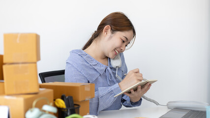 Young woman selling products online was talking on the phone to receive an order from a customer who called and wrote down the list in a notebook, New kind of business for young, Sell online.