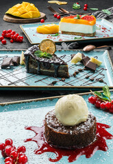 Wall Mural - Variety of summer desserts, brownie with ice cream, mango cheesecake, and chocolate layer cake on a dark background close up view. Summer desserts and sweets