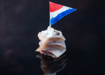 Traditional local food. Pieces of herring on a dark background with the flag of the Netherlands.