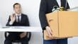 © Puwasit Inyavileart - Young woman wearing a black suit raises a brown cardboard box from the office, Businessmen pack personal belongings and equipment after Resign or being fired, Employment contract is expire.