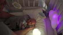 Father Puts His Baby Boy In A Crib 3-week-old Newborn In Bed With Musical Mobile Carousel