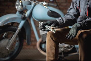 Wall Mural - A mechanic with a wrench in hand is sitting on the broken motorbike background and is spreading his hand. Motorcycle repairing service concept.