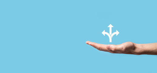 Male hand holding icon with three directions icon on blue background. Doubt, having to choose between three different choices indicated by arrows pointing in opposite direction concept. Ways