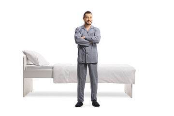 Wall Mural - Full length portrait of a young man in pajamas standing in front of a single bed