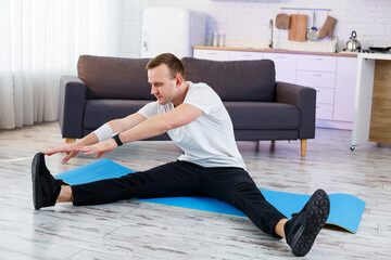 Wall Mural - Muscular athletic man in a t-shirt doing warm-up exercises at home. Doing sports at home during the quarantine period. Fitness outside the gym