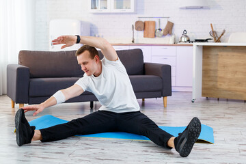 Wall Mural - Muscular athletic man in a t-shirt doing warm-up exercises at home. Doing sports at home during the quarantine period. Fitness outside the gym