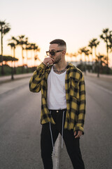 Wall Mural - Vertical shot of a handsome Spanish Caucasian man with tattoos and sunglasses posing outdoors