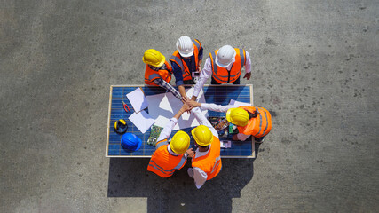 Wall Mural - Top view of Architectural engineers putting their hands together on solar panel and his blueprints with Solar photovoltaic equipment on construction site. meeting, discussing, designing, planing