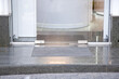 granite gray porch step with a foot mat at the entrance to the central door made of tempered glass on floor iron hinges modern architecture office style close-up, nobody.
