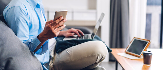 Young smiling asian man relaxing using laptop computer working and video conference meeting at home.Young creative man looking at screen typing message with smartphone.work from home concept