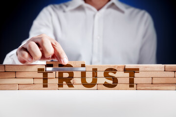 Businessman builds a structure of wooden blocks with the word trust. Building trust in business