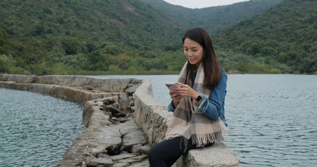 Wall Mural - Woman use of mobile phone and sit beside the sea