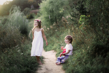 Cute romantic children a couple, a boy plays the guitar and sings, a girl in a dress is dancing. Children in a summer park barefoot on the grass. happy carefree childhood and romance